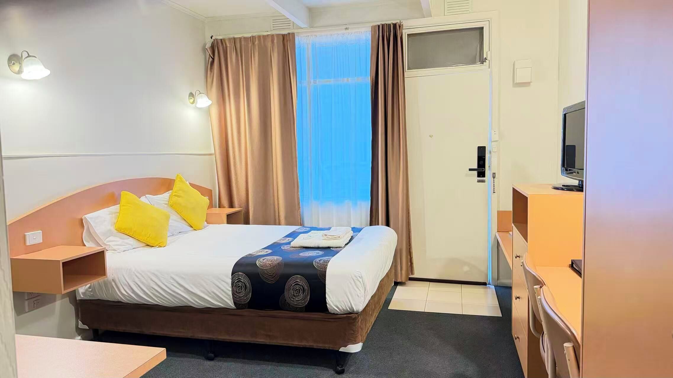 Quarto de hotel com uma cama, duas mesas de cabeceira, uma televisão e uma janela com cortinas.