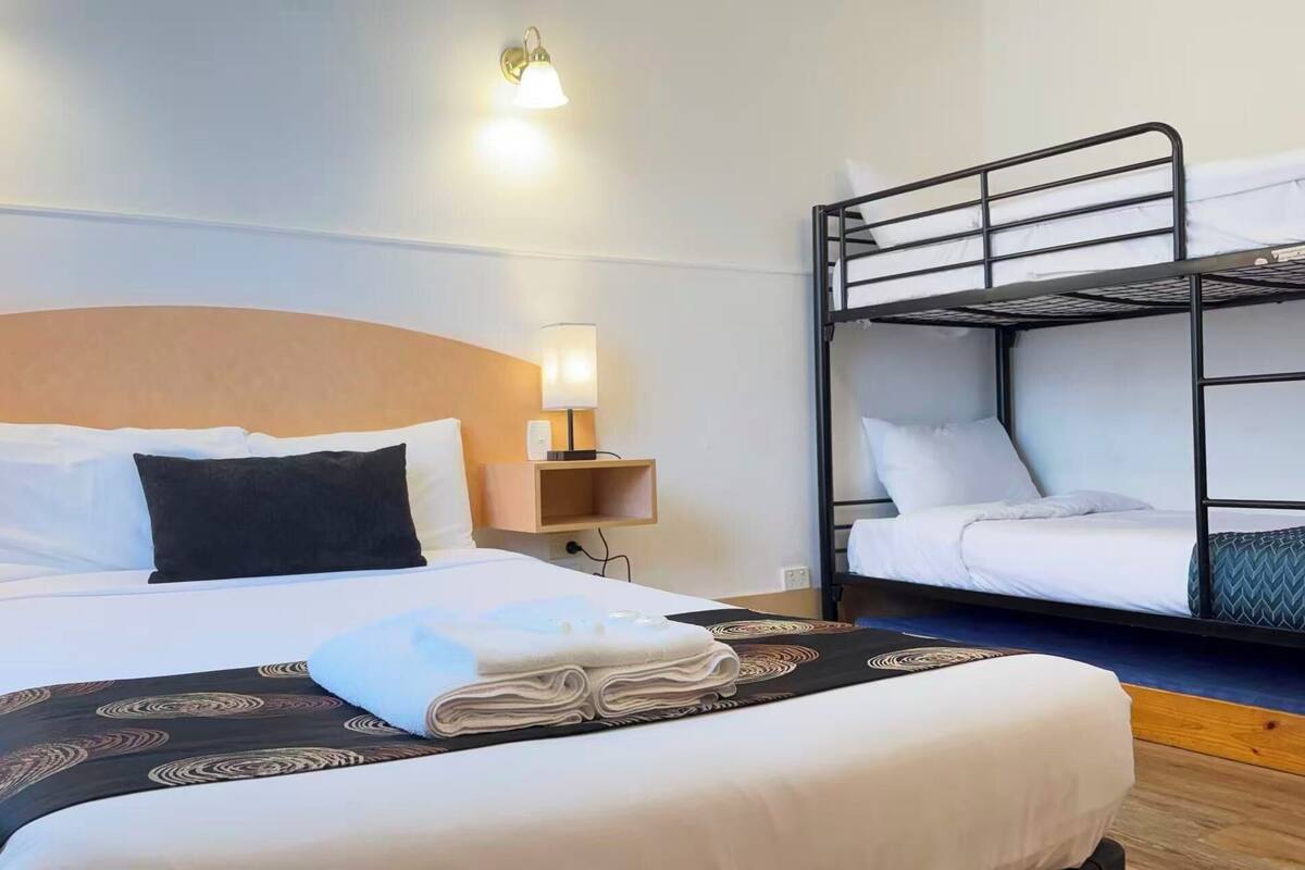 A hotel room with a single bed, a bunk bed, bedside lamps, and a wall-mounted light fixture.