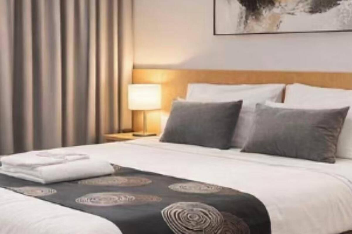 A hotel room with a bed, a nightstand, a lamp, a painting on the wall, and a window with curtains.