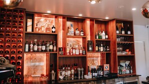 Zona de bar con estantes llenos de botellas de licor y vasos, una cava de vinos y un cartel que indica que no se permite fumar.