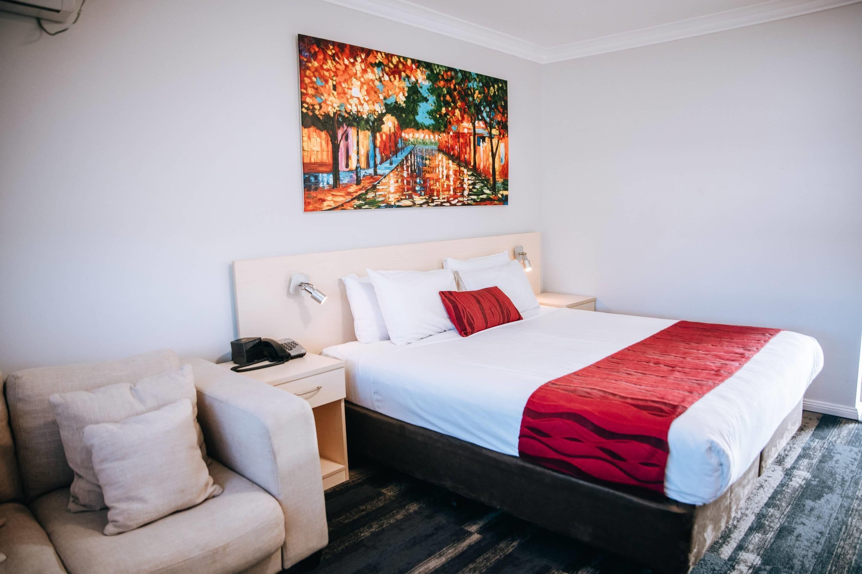Un cuarto de hotel con una cama grande, una mesita de noche, una silla y un cuadro en la pared.