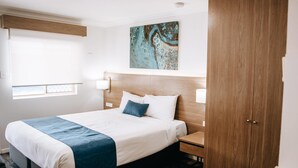 Habitación de hotel con una cama grande, cabecera de madera, un cuadro en la pared, una ventana y un armario.