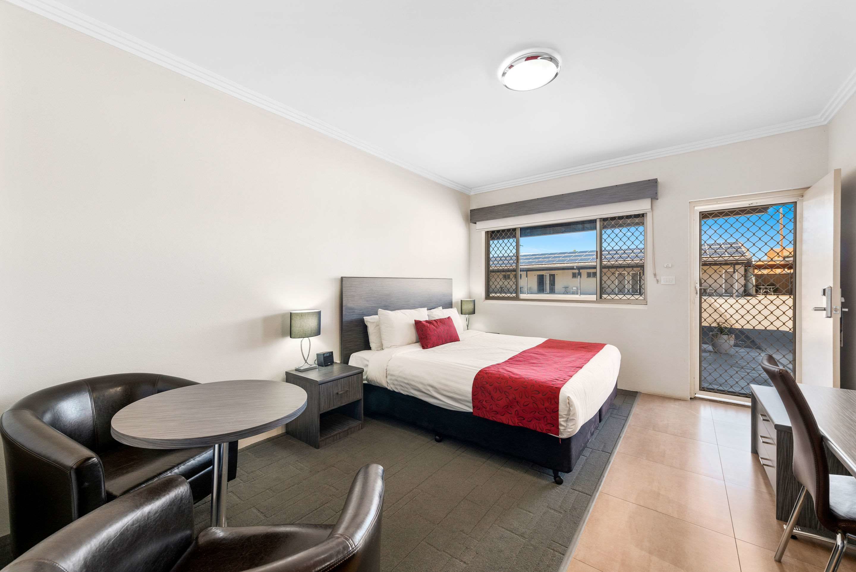 Habitación de hotel con una cama, un escritorio, una silla, una mesita y una ventana.