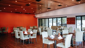Un comedor amplio con varias mesas y sillas, techo de madera y ventanas grandes que dejan entrar luz natural.