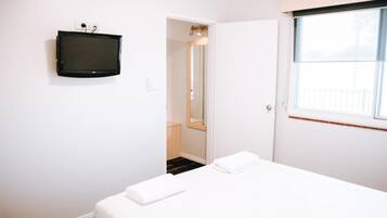 A hotel room with a bed, a television mounted on the wall, a window, and a door leading to another room.