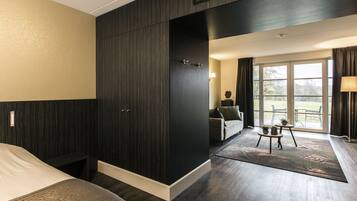 Een hotelkamer met een groot bed, een donker houten garderobe, een klein tafeltje met planten en uitzicht op het landschap door een groot raam.