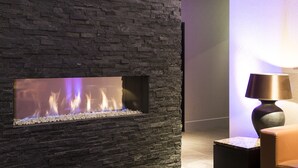A modern interior with a stone wall, a built-in fireplace, and a lamp.