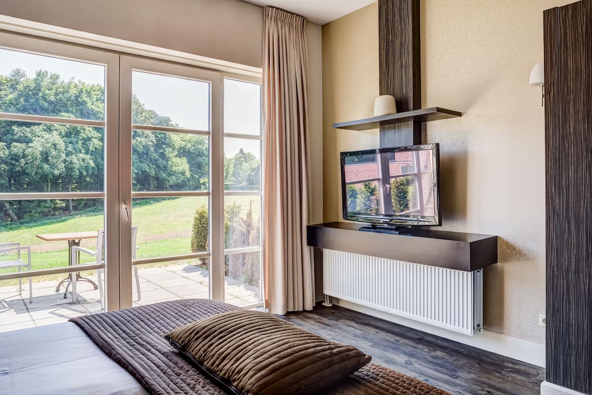 Een slaapkamer met een groot raam, een televisie en uitzicht op een groen landschap.