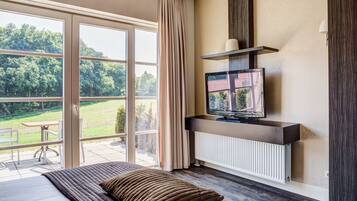 Un dormitorio con un ventanal grande, televisión y vistas a un paisaje verde.