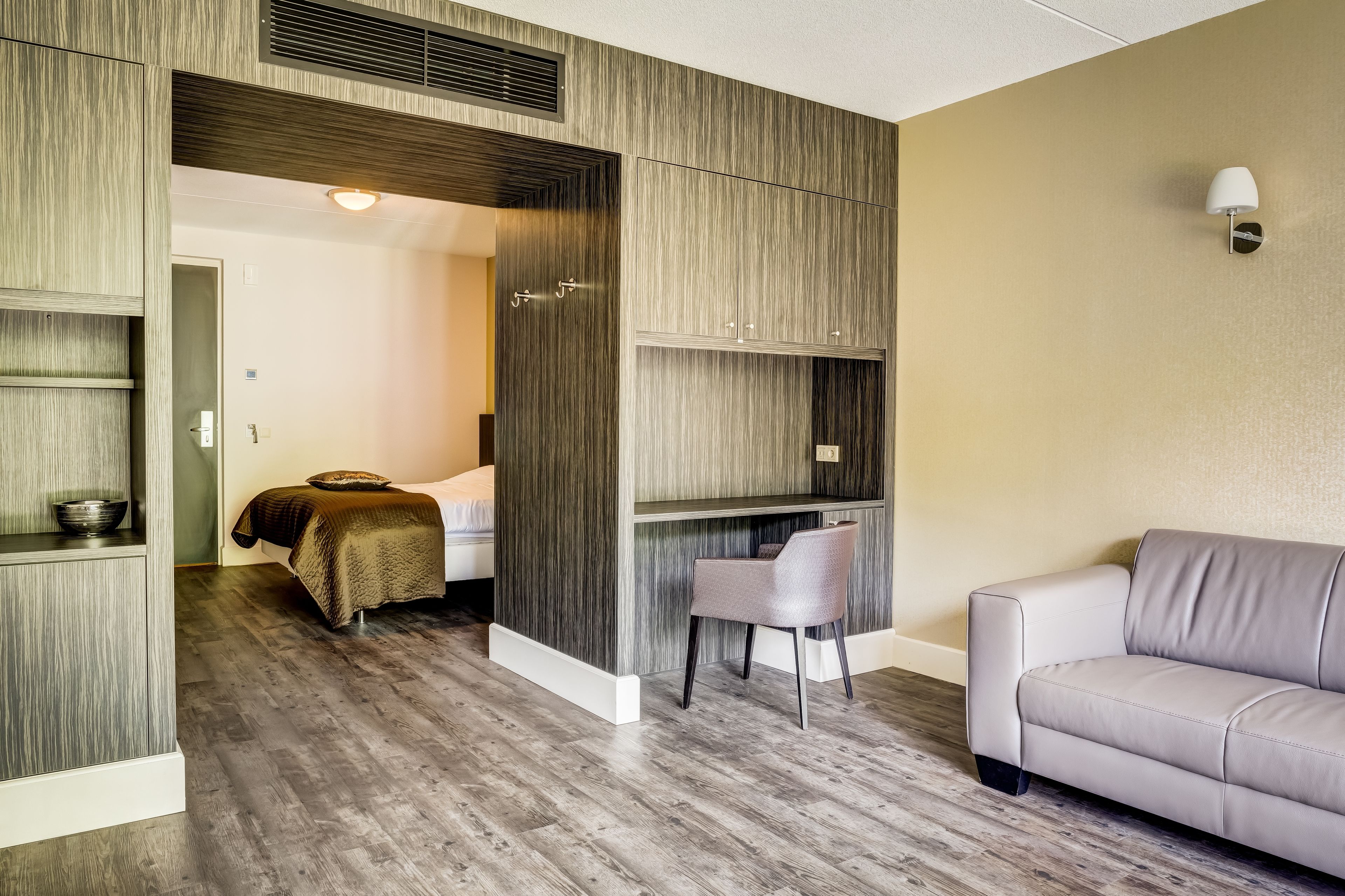A modern room with a bed, a grey sofa, a chair, and built-in shelving.