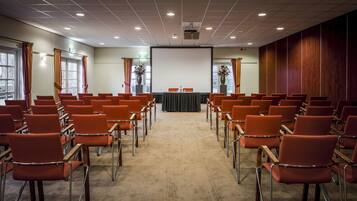 A conference room with rows of orange chairs, a projector screen, and a table with a black tablecloth.