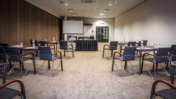 Une salle de conférence dotée d’un grand écran, de plusieurs tables avec des chaises et d’un sol recouvert de moquette.
