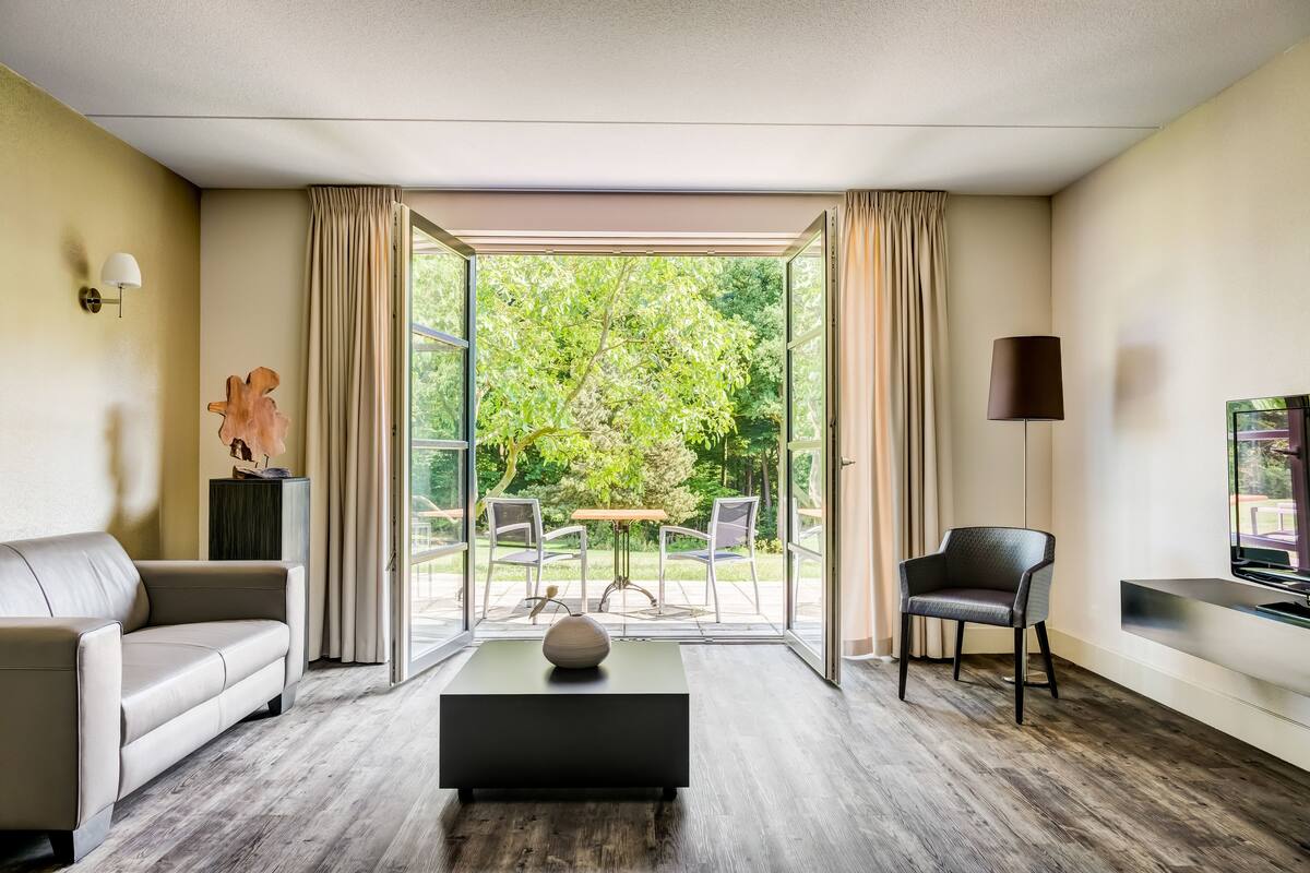 Een moderne woonkamer met een bank, een salontafel, een televisie en uitzicht op een tuin door een glazen deur.