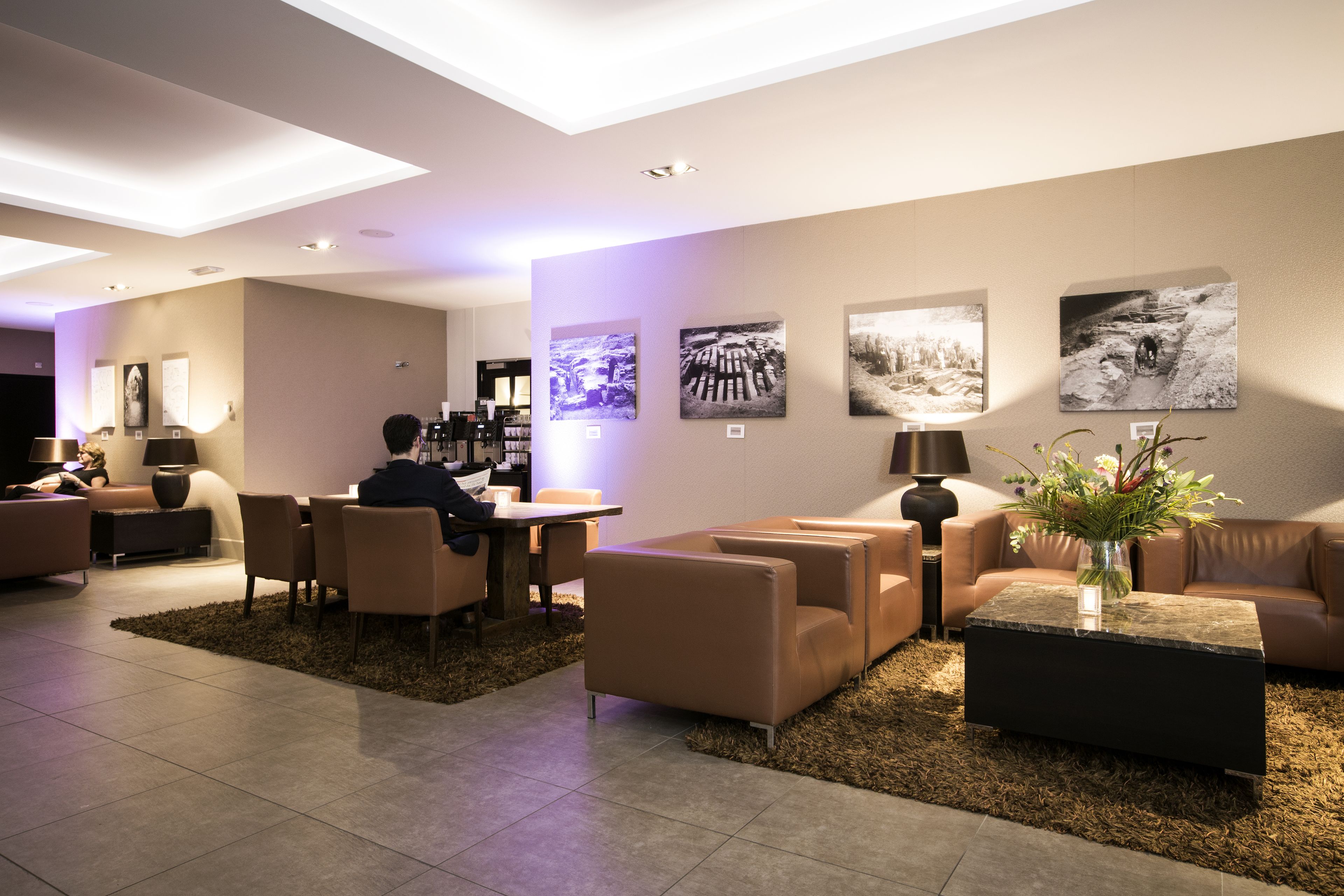 A modern hotel lobby with a seating area, a coffee table with a vase, and wall-mounted artwork.