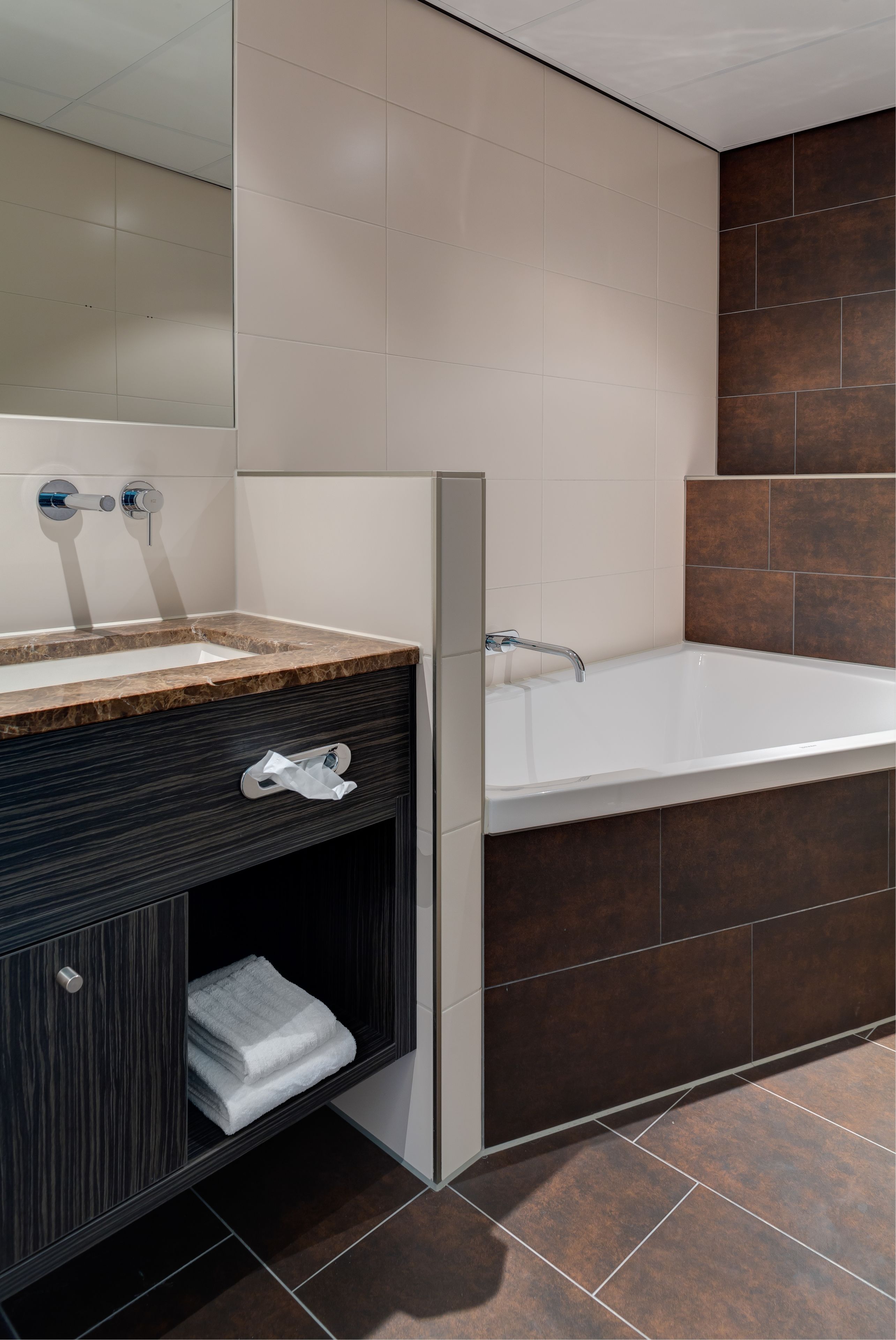 A modern bathroom with a marble sink, a large bathtub, and dark wood cabinetry.