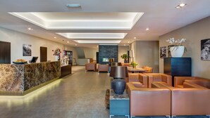 A modern hotel lobby with a marble reception desk, leather seating, a large vase with flowers, and artwork on the walls.