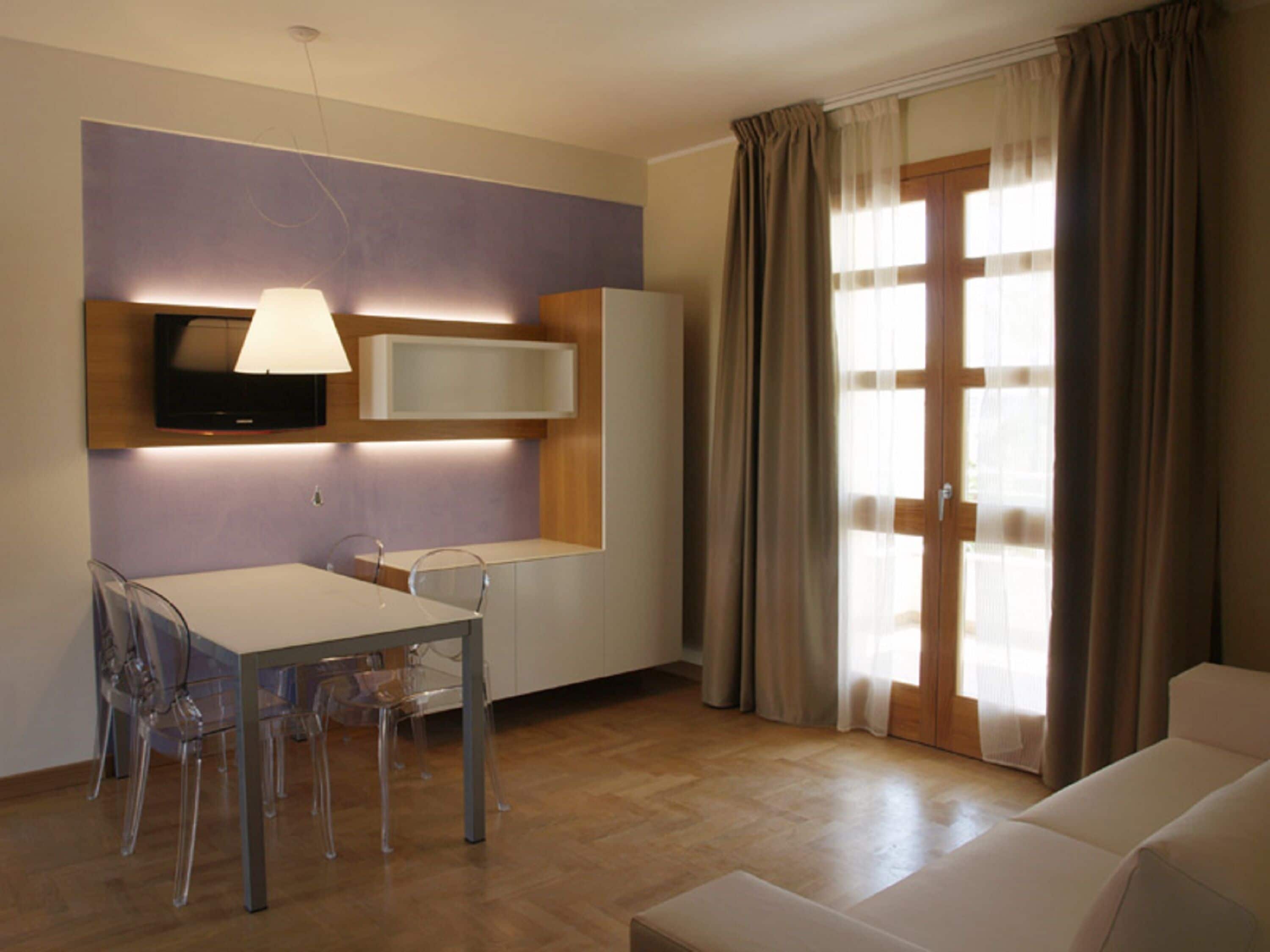 Una sala de estar moderna con comedor, un televisor de pantalla plana en la pared y un ventanal corredizo que da a un balcón.