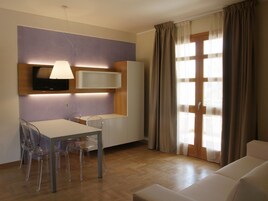 Una sala de estar moderna con comedor, un televisor de pantalla plana en la pared y un ventanal corredizo que da a un balcón.