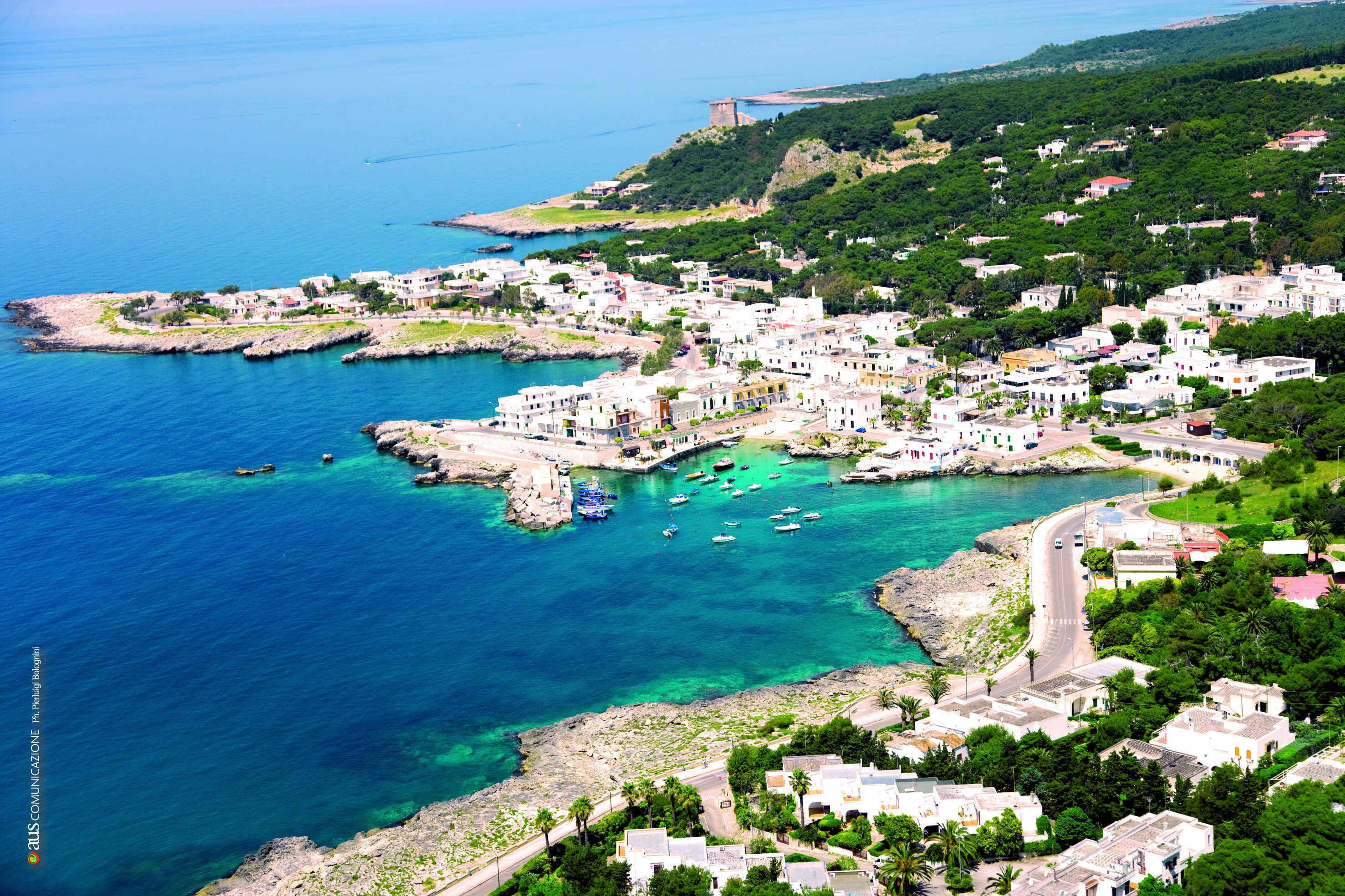 A coastal town with buildings along the waterfront, clear blue waters, and a hilly backdrop.