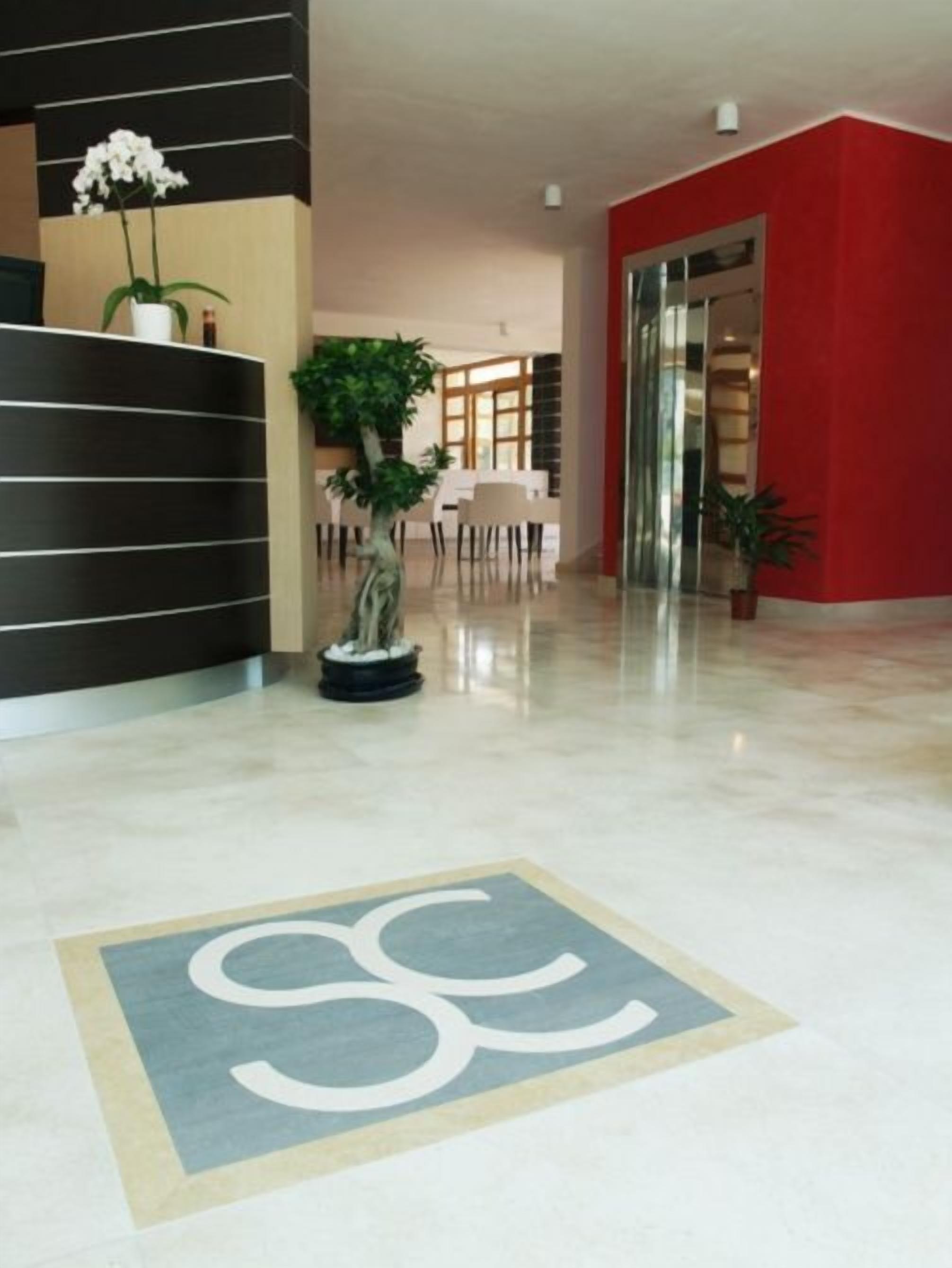 Un hall d’entrée moderne avec un comptoir de réception, une plante en pot, un espace repas et un mur d’accent rouge.