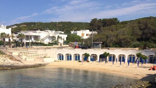 Zona costera con agua cristalina, una playa de arena y un edificio con puertas azules.