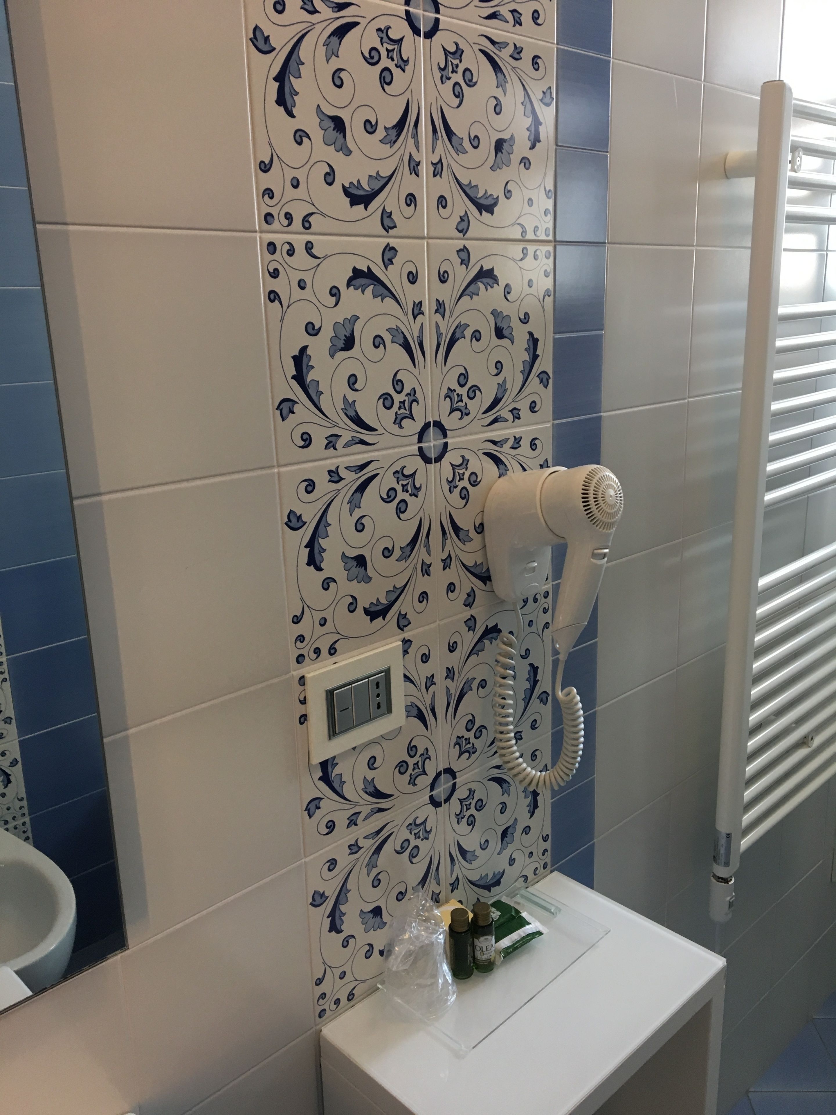 A bathroom with a patterned tile wall, a white sink, and a towel rack.