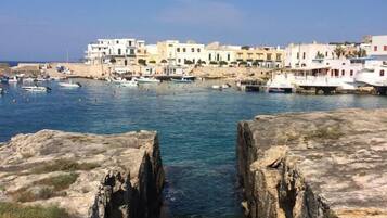 A coastal town with stone steps leading to a harbor, surrounded by buildings with balconies and a clear blue sky.