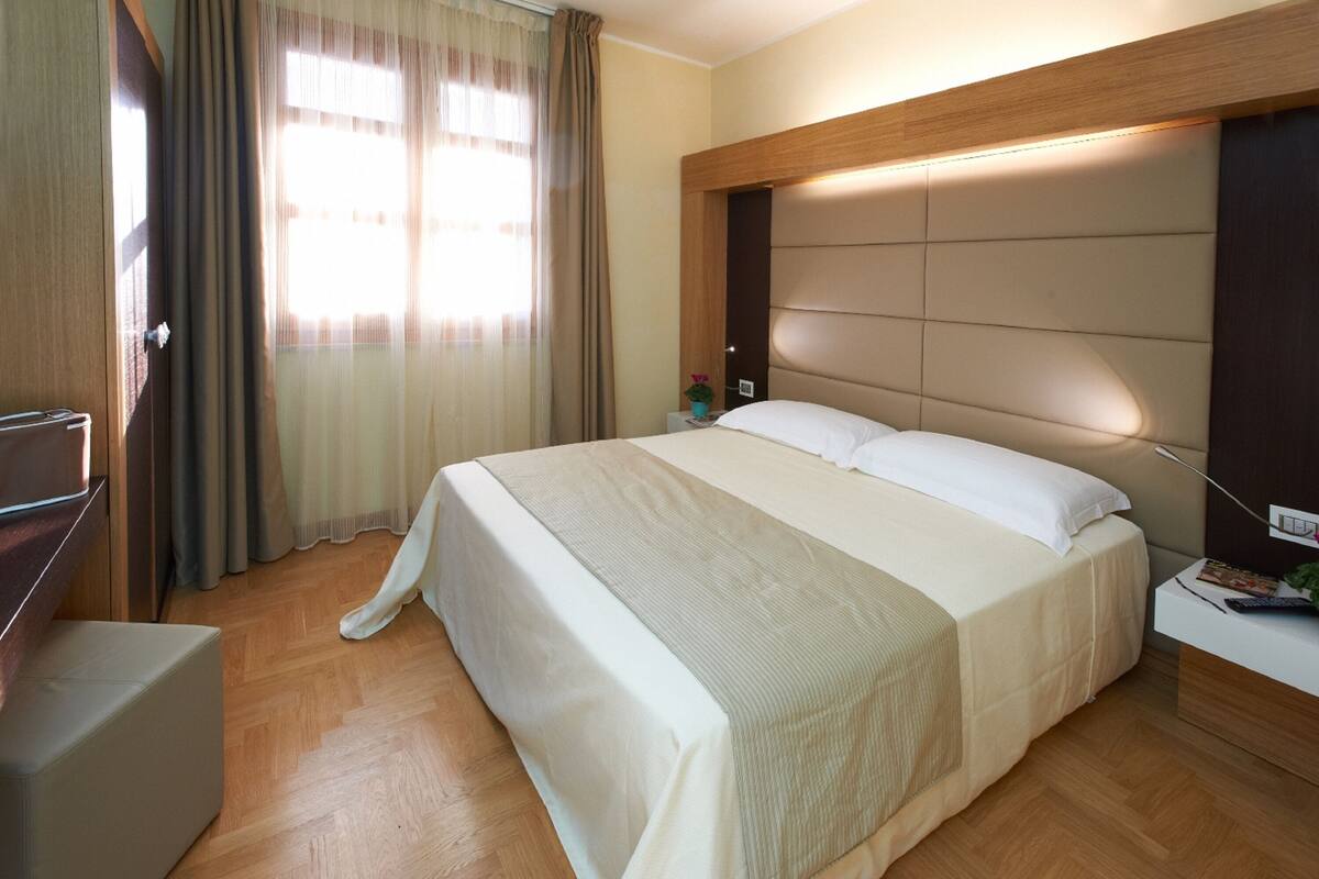 A hotel room with a large bed, wooden headboard, and a bedside table with a lamp.