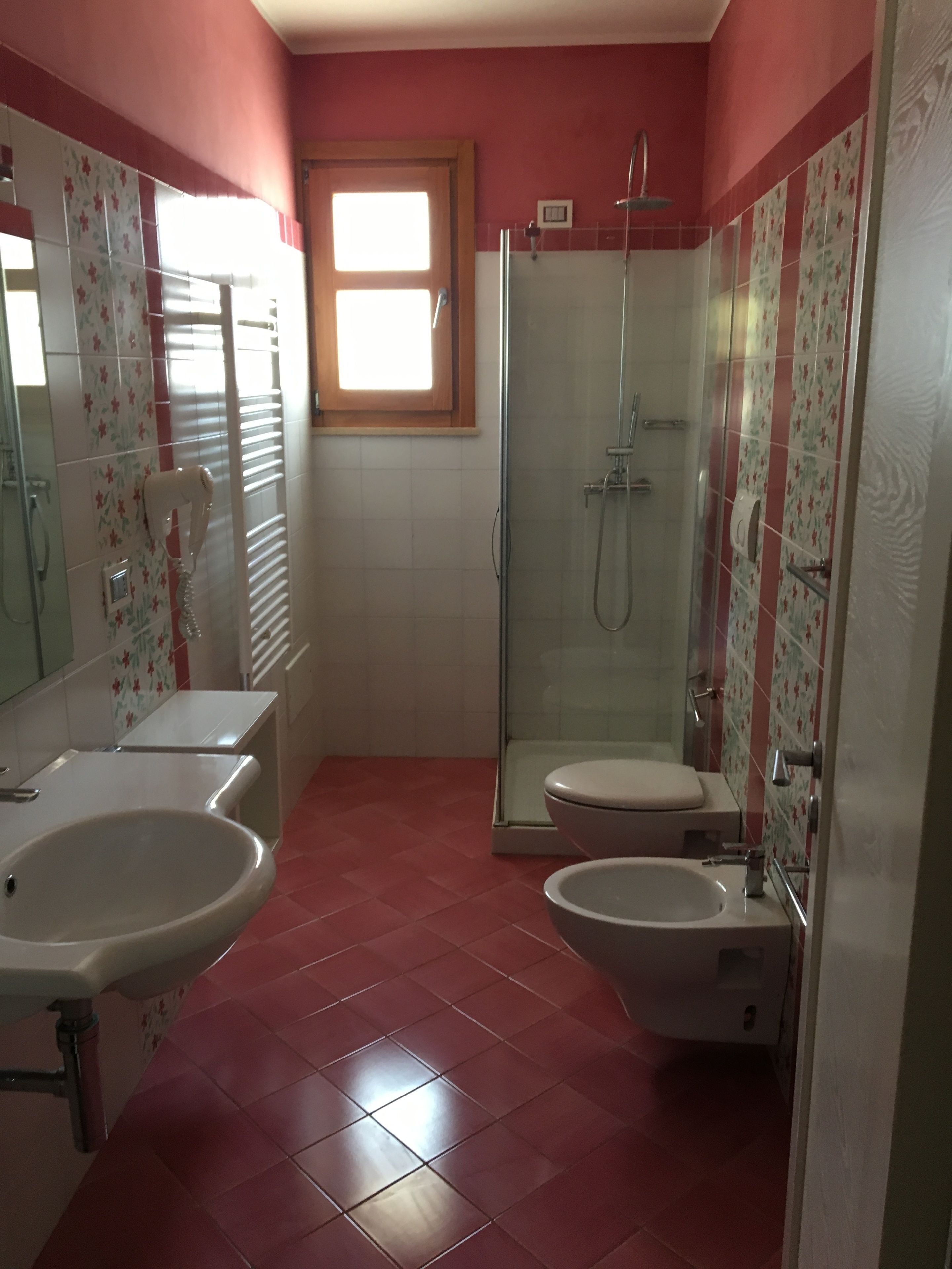 Een badkamer met een douche, twee wastafels, een toilet en een raam.