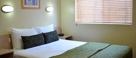 A neatly made bed with white and patterned pillows, a green patterned bedspread, and a bedside table with a lamp.