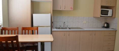 Una cocina compacta con armarios de madera, un refrigerador blanco, un microondas y un lavamanos.