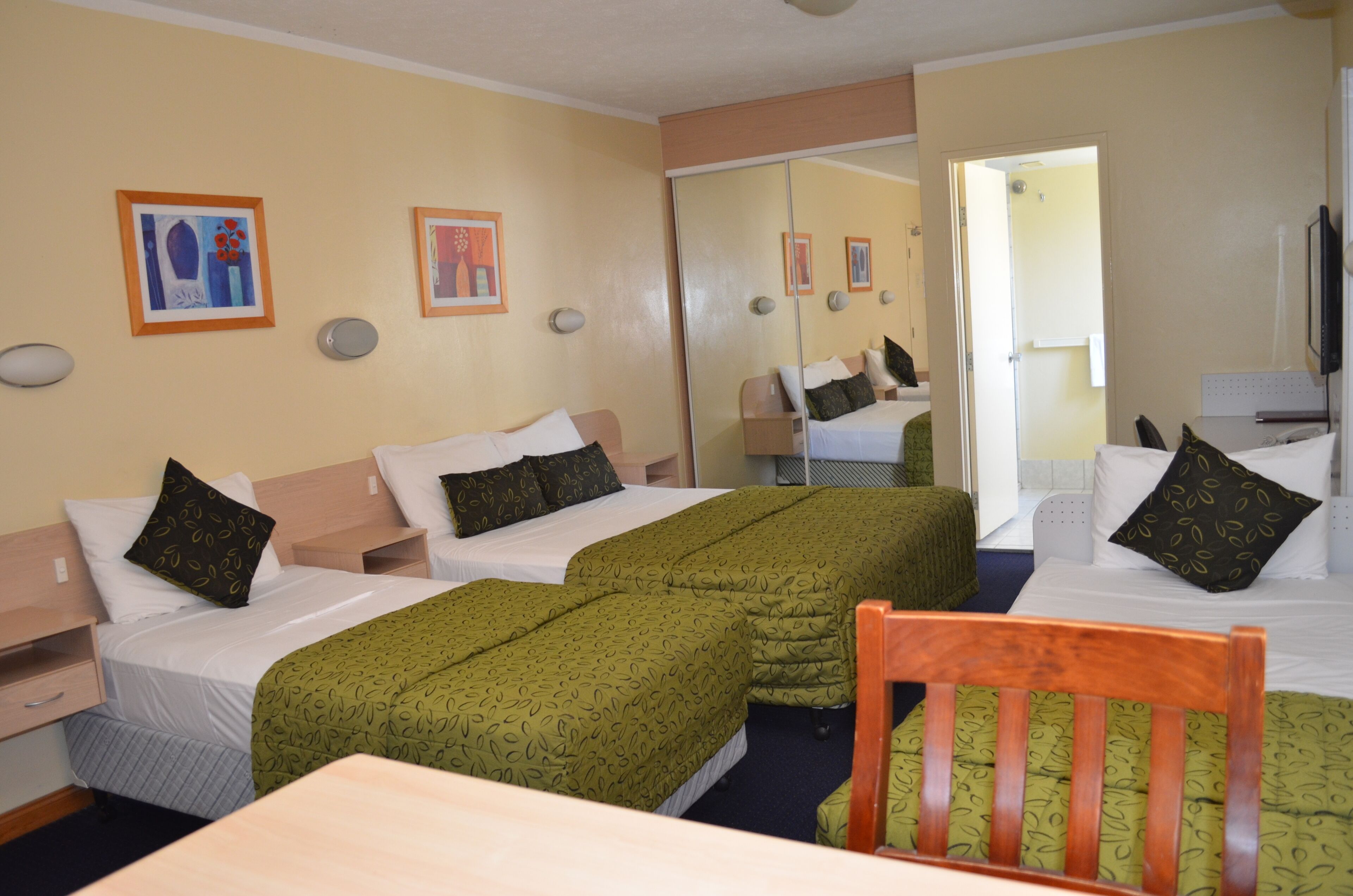 A hotel room with two single beds, a wooden chair, a table, and artwork on the walls.