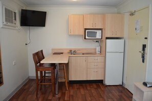 A compact kitchen with wooden cabinets, a microwave, a refrigerator, a dining table with chairs, and a TV mounted on the wall. - Airport Motel (Hamilton)