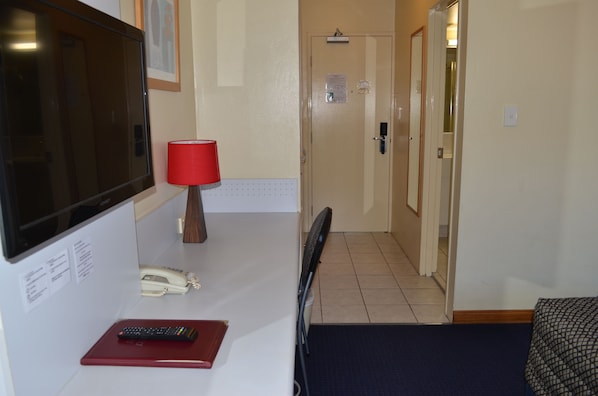 A hotel room with a bed, a desk with a TV, a telephone, and a red lamp. - Airport Motel (Hamilton)