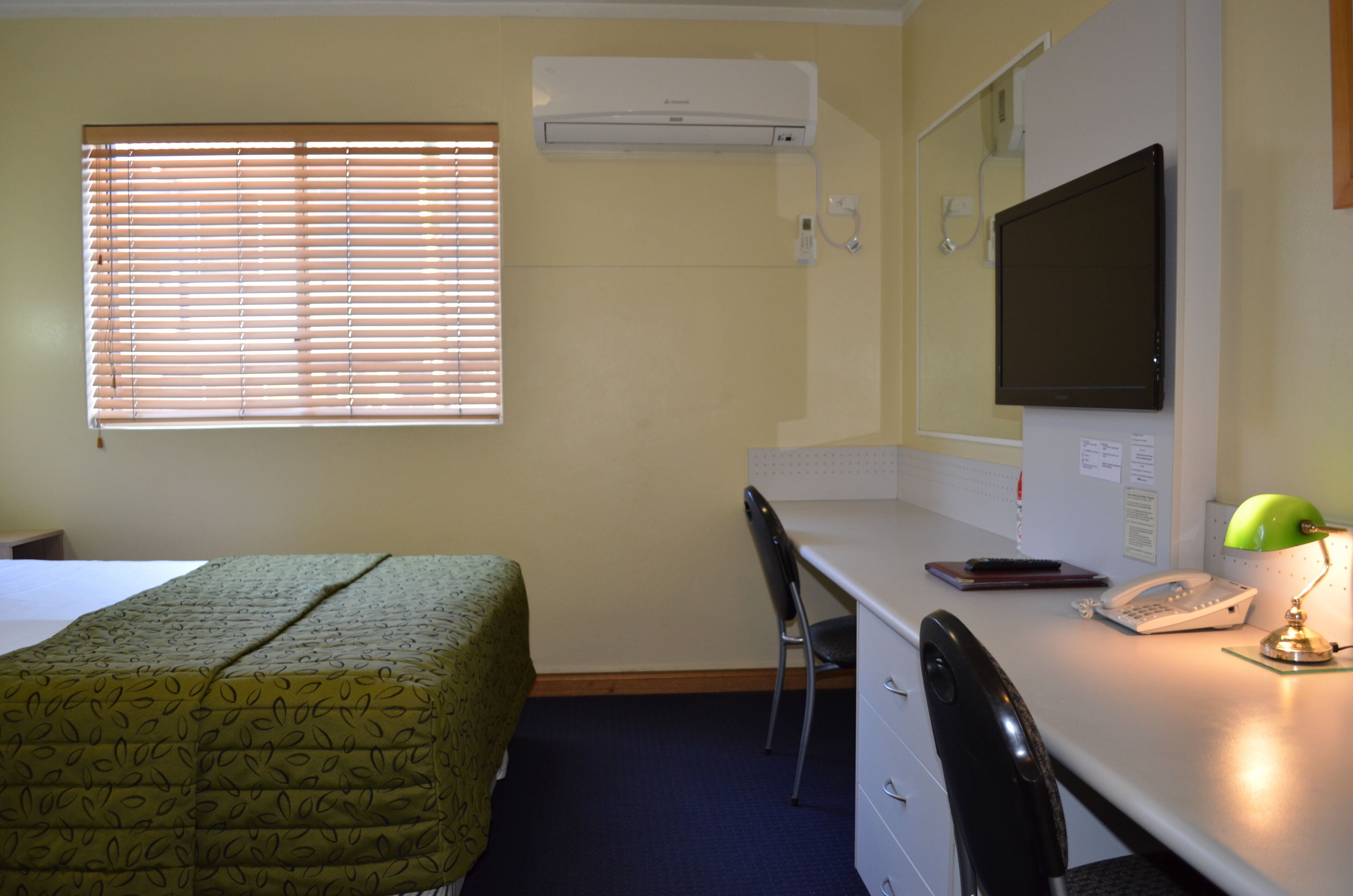 Une chambre d’hôtel équipée d’un lit, d’un bureau, d’une chaise, d’un climatiseur et d’un téléviseur.
