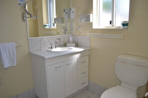 A bathroom with a white sink, mirror, and toilet. There are two hair dryers mounted on the wall above the mirror. - Airport Motel (Hamilton)