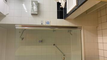 Une salle de bain moderne avec une douche à parois de verre, des murs recouverts de carreaux blancs et un plan de toilette où sont posés les articles de toilette.