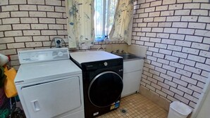 Un lavadero con lavadora, secadora, lavamanos y un cubo de basura.