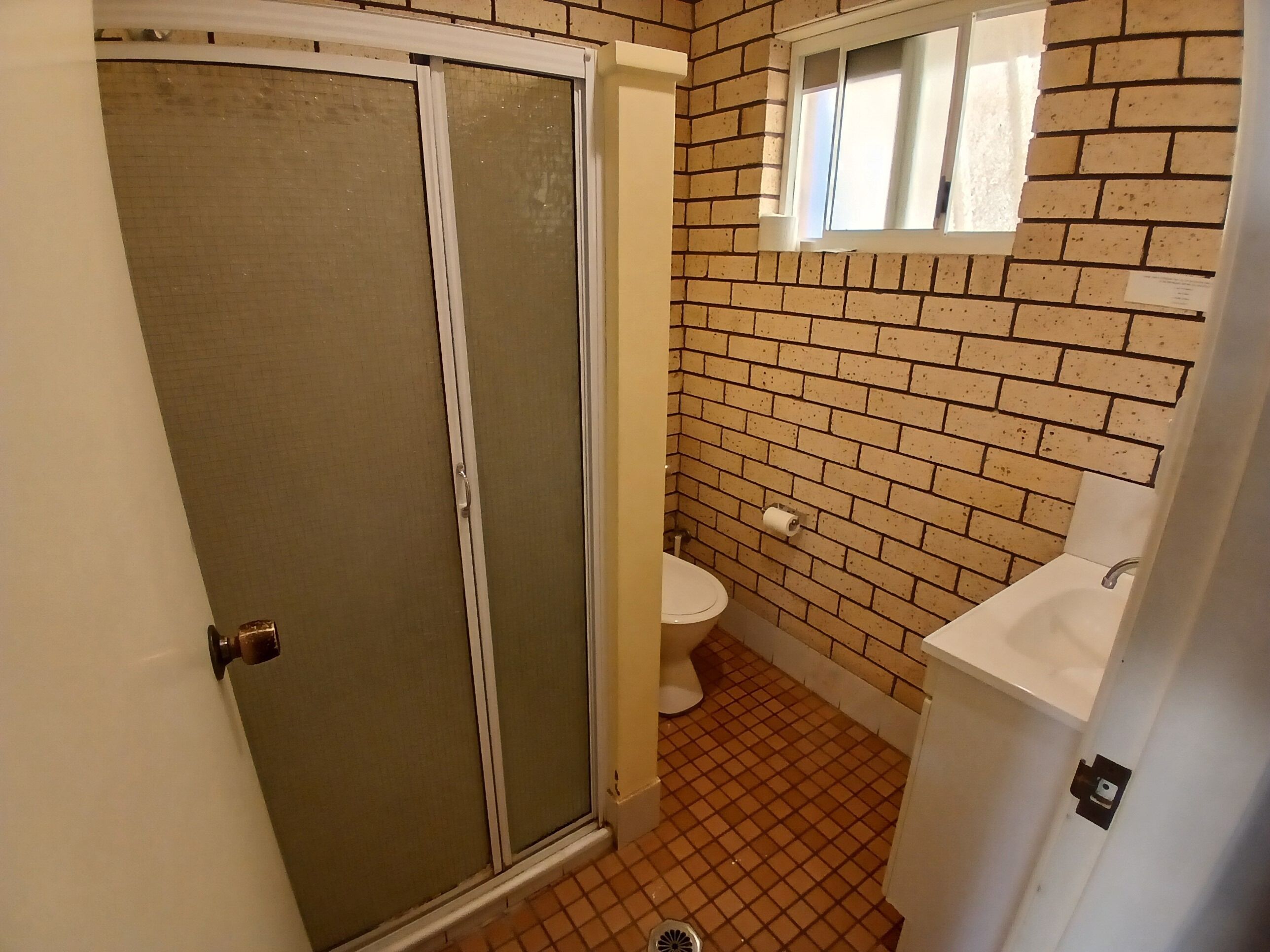 Baño con inodoro, lavabo y ducha con puerta de vidrio.