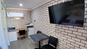Cocina compacta con microondas, refrigerador y una pequeña mesa de comedor con sillas. Un televisor de pantalla plana está montado en la pared.