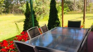 An outdoor patio with a glass-top table and four chairs, surrounded by greenery and a wooden pergola. - Alexanders' Of Richmond (Richmond)