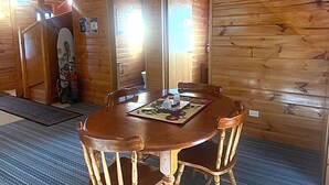 A wooden cabin interior with a dining table, chairs, a surfboard, and a visible bathroom door. - Alexanders' Of Richmond (Richmond)