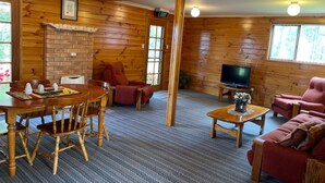 A cozy cabin interior with a wooden dining table, two chairs, a sofa, a television, and a fireplace. - Alexanders' Of Richmond (Richmond)