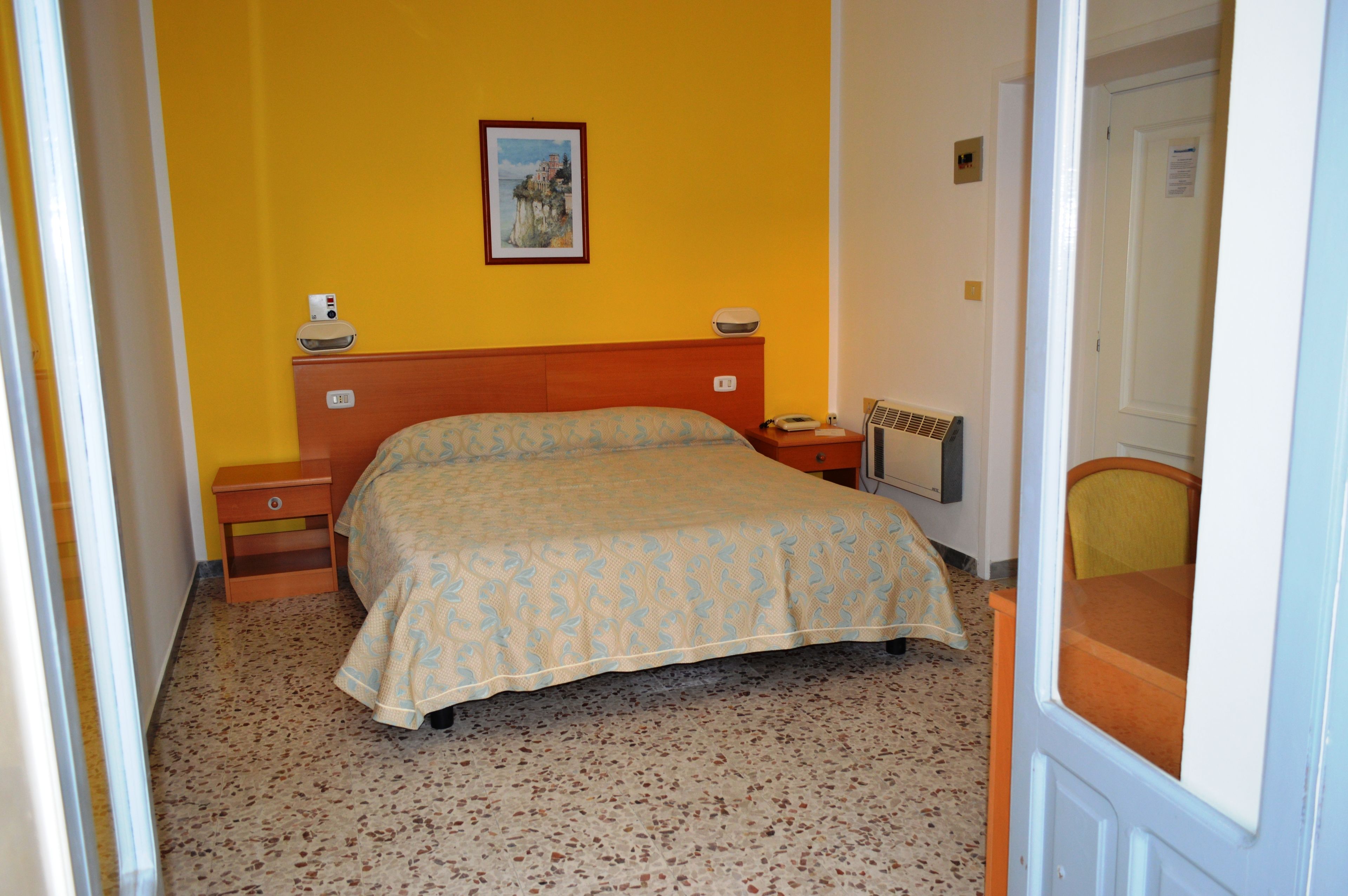 Une chambre à coucher avec un lit, des tables de chevet, une commode, un radiateur et un tableau au mur.