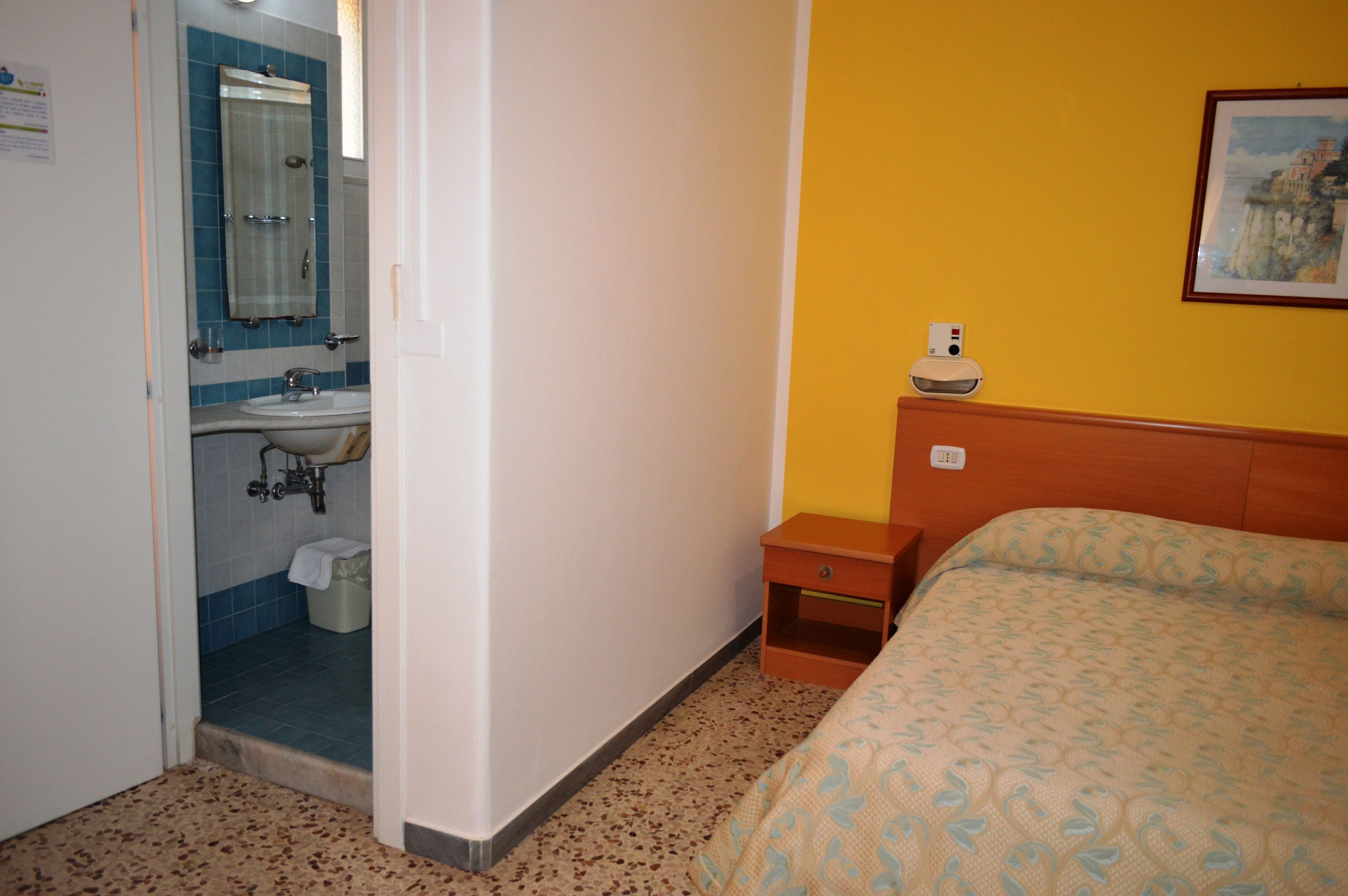 A hotel room with a bed, a nightstand, a small table, a sink, and a mirror.