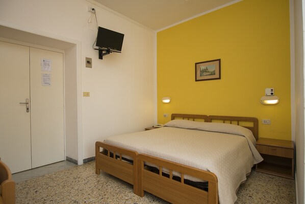 A bedroom with a bed, a television mounted on the wall, and a door with a handle. - Albergo Delfino (Camerota)