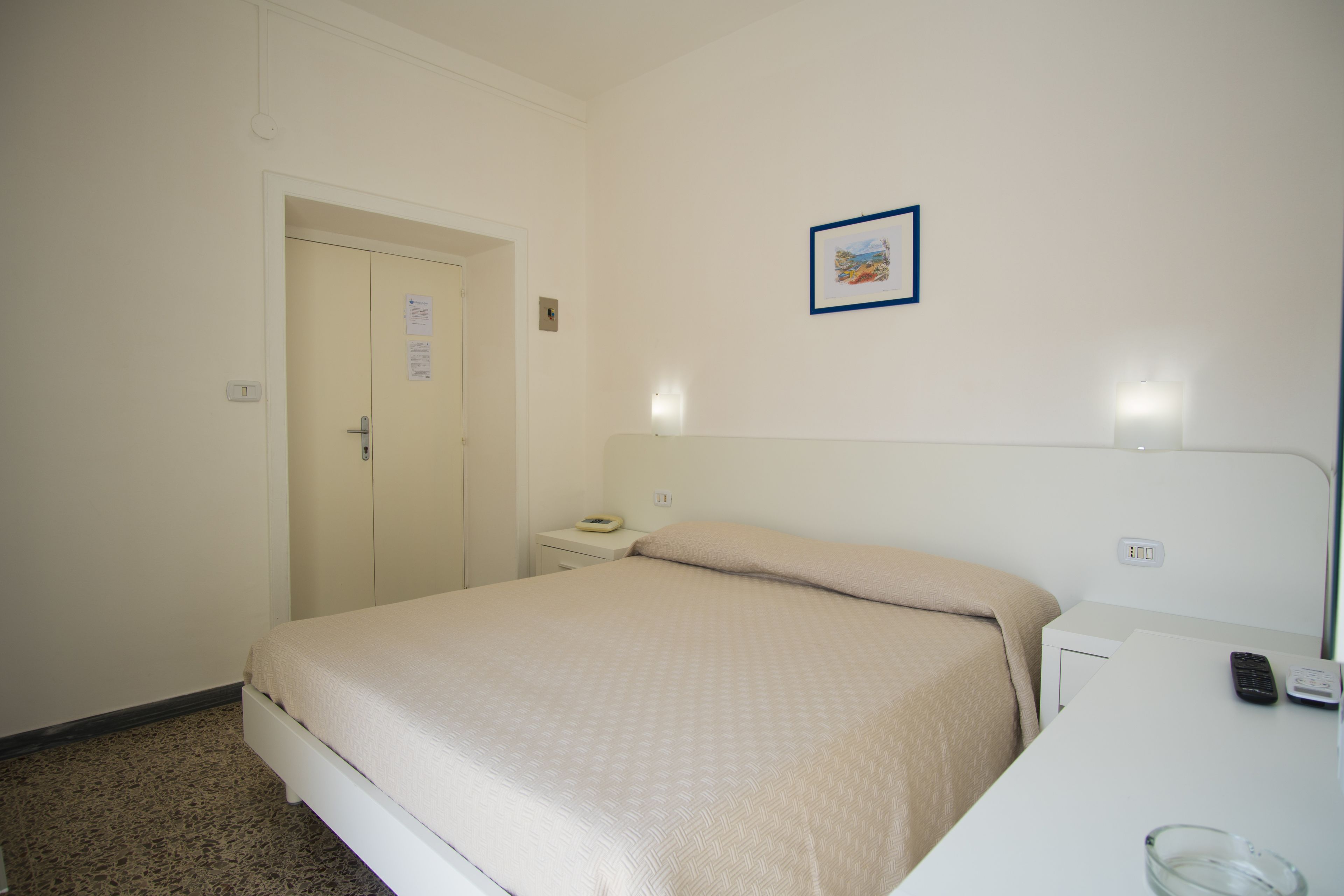 A hotel room with a bed, bedside table, and a small desk with a chair.