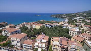 Una cittadina costiera con edifici, un mare blu cristallino e un paesaggio collinare sullo sfondo.