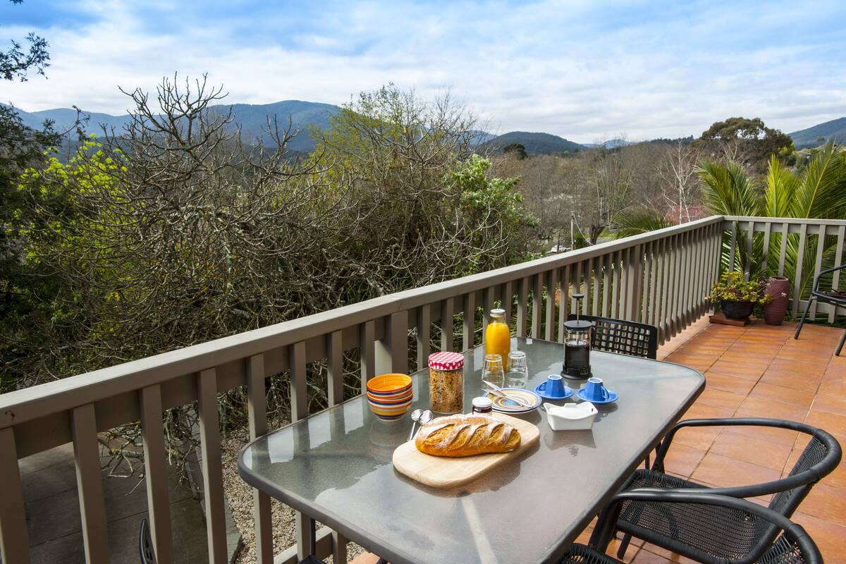 A balcony with a table set for breakfast, overlooking a mountainous landscape.