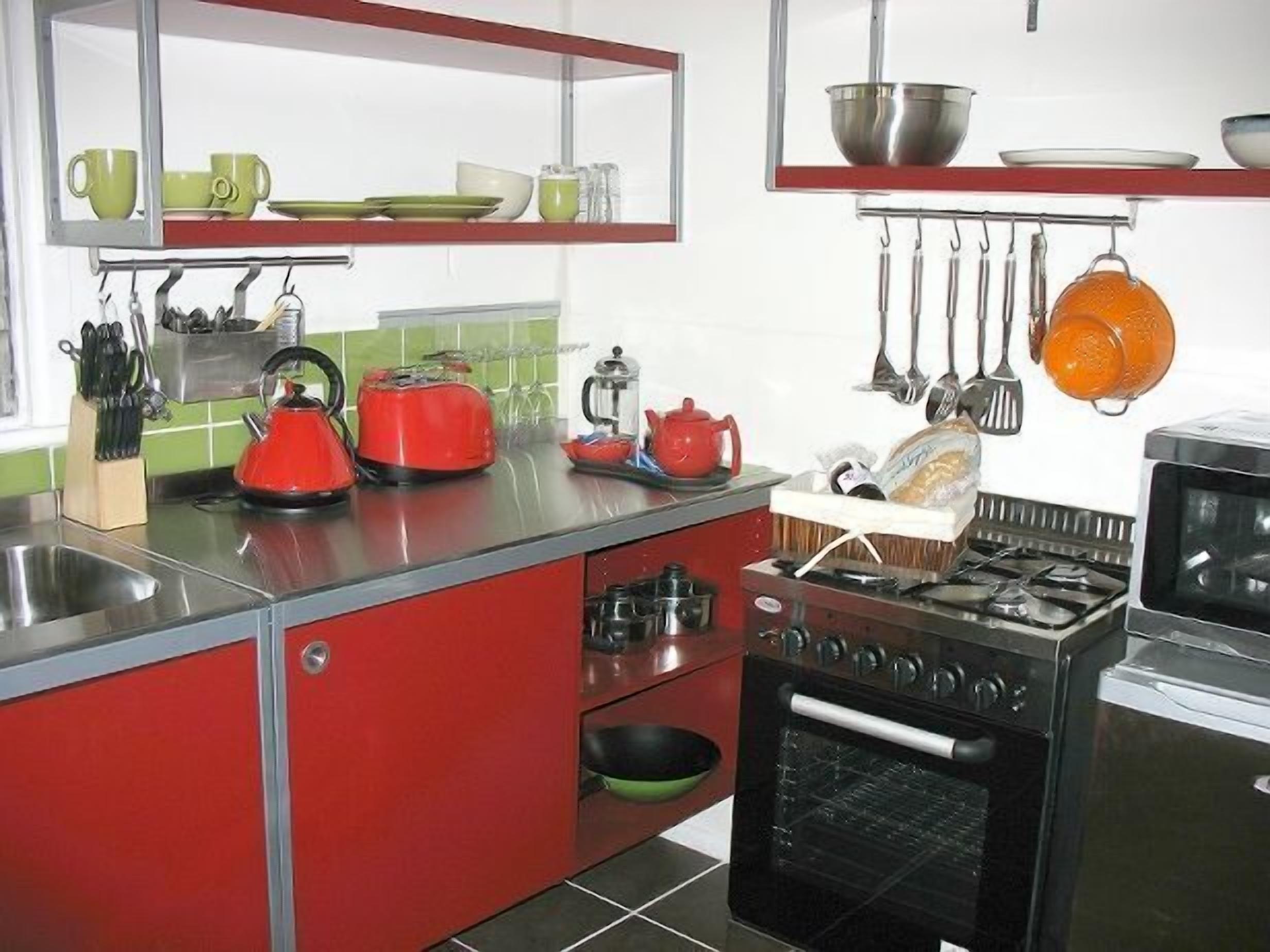 A kitchen with red cabinets, a gas stove, an oven, and various utensils hanging above the counter.